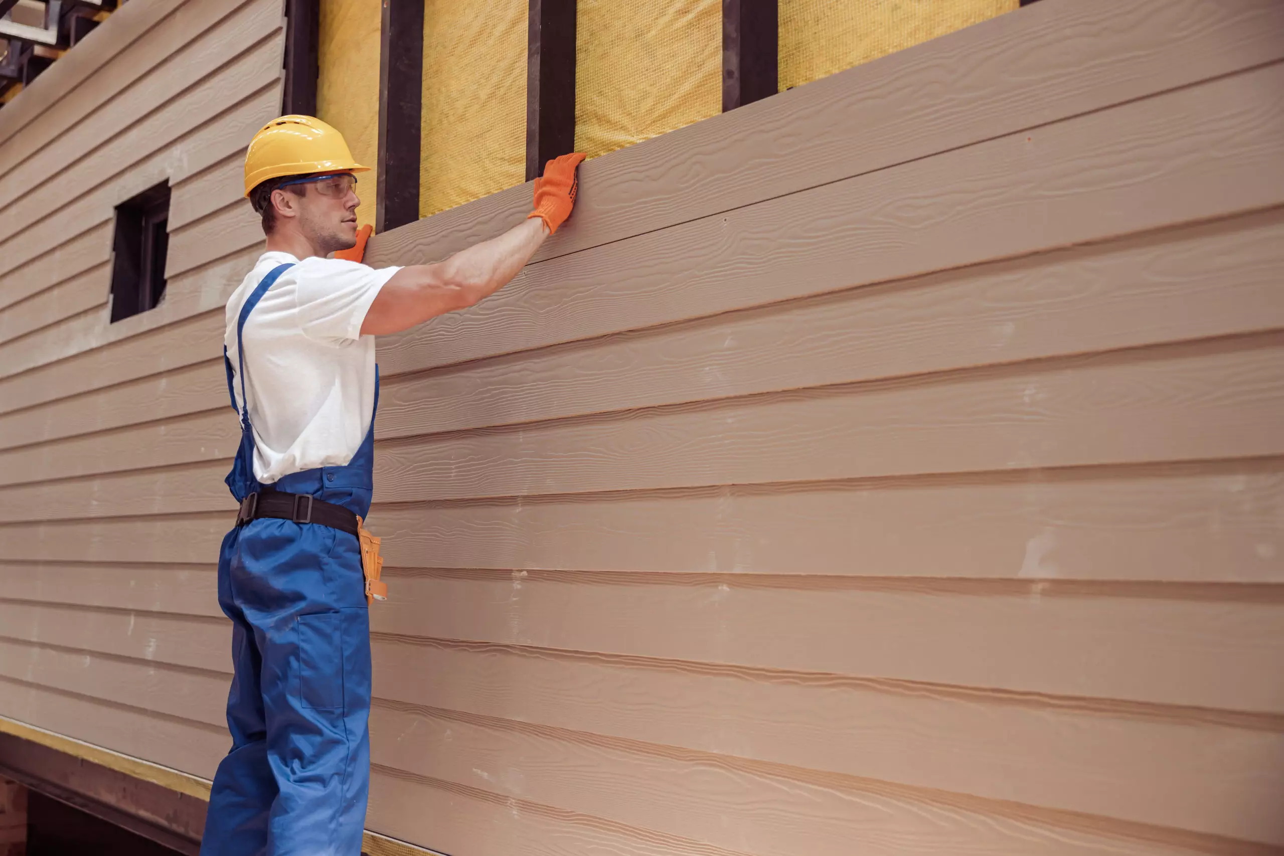 Male worker building house at construction site, placing siding on house
