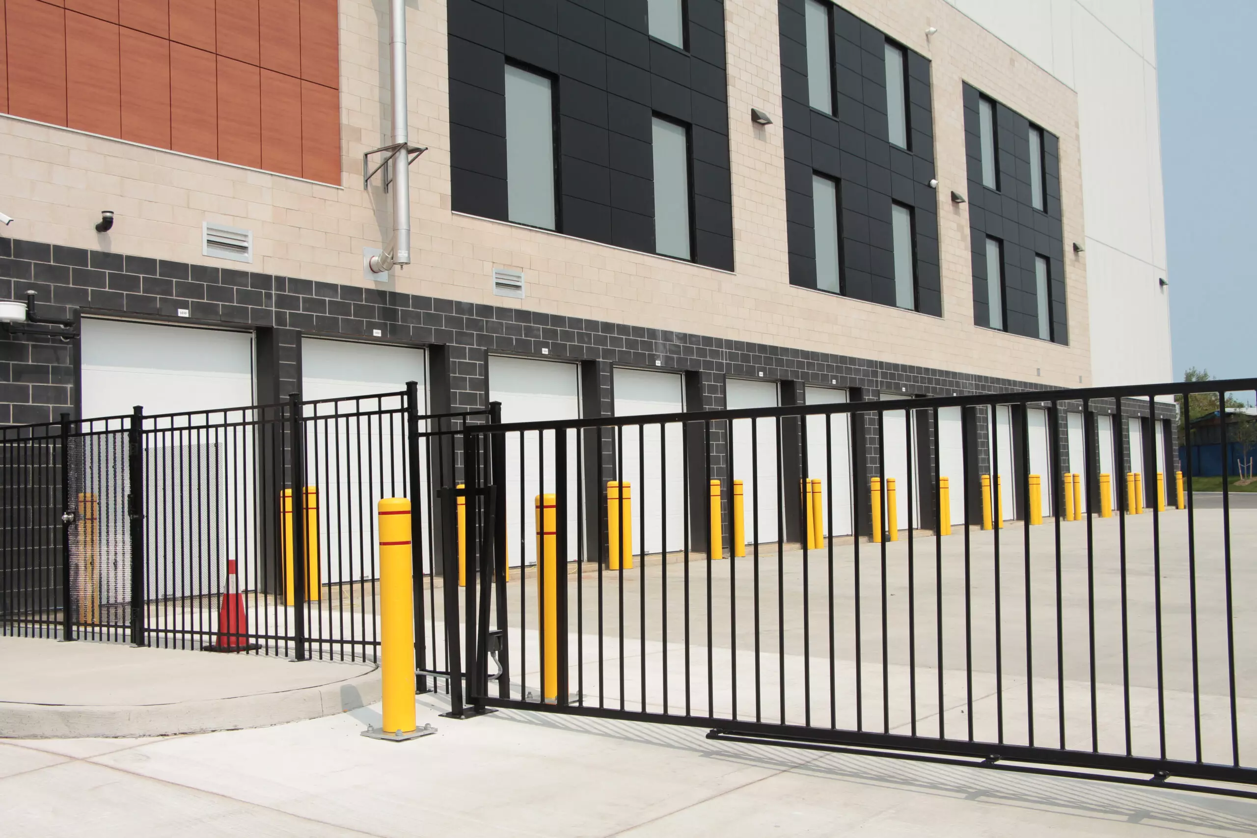 line row of exterior outdoors outside building public storage white garage units behind black metal fence mechanical gate on cement pavement